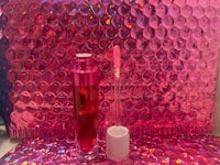 a bottle of lipgloss sitting on top of a pink background