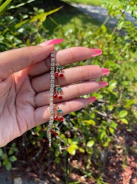 a hand holding a bracelet with red cherries on it